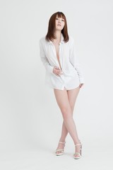 白いシャツを着たセクシーな女性。この女性は、脚の素肌を見せています。スタジオ撮影、白背景。