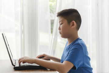 Young Asian boy using laptop technology at home.