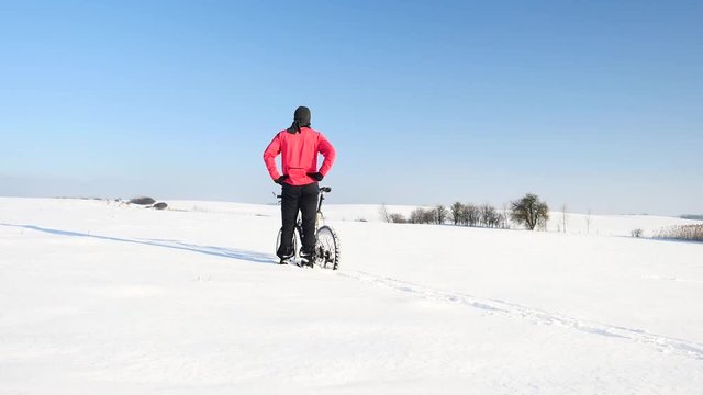 Man biker push mountain bike in powder snow. Alone man in pink black sportswear is pushing bike in fresh deep snow drift. Freeze sunny winter day with small snow flakes in the air.