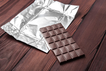 Chocolate bar in wrapper on the dark wooden background.
