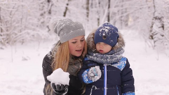 Happy family of mother with kid playing in the snow winter park.