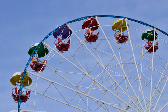 The upper part of the ferris wheel in the winter.
Colorful Ferris wheel cabins that are covered with snow against the blue sky.