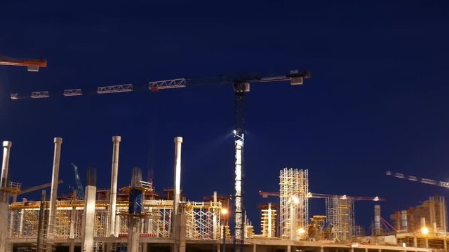 Timelapse with cranes working on construction site on night sky background. Concept of working construction yard.