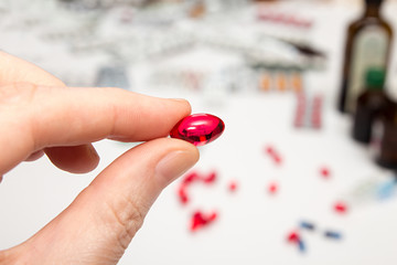 Red capsule with vitamins in fingers. Hand holding pills.
