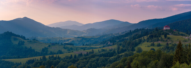 Fototapeta premium Wide sunset panorama of the Carpathian mountains. Ukraine. Small hotel on hill at the right part of image as detail.