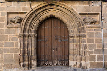 Puerta antigua de madera con arco de piedra y esculturas.