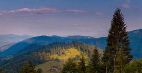 Carpathian mountain slopes in the sunrise rays. Rural house on green hill.