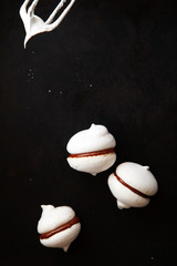 Three white meringue cookies and mixer whisk on black background