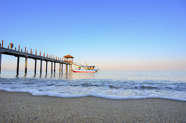 Old jetty with fisherman buat during blue sky.