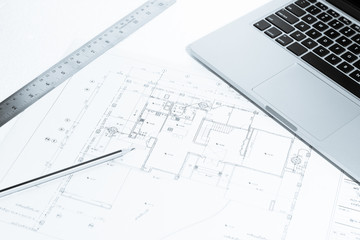 Pen, metal ruler, and notebook over house construction blueprint