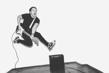 Awesome crazy fashion young musician rock guitar player jumps with passion in studio. Stylish rocky emotional man. Black and white toned.
