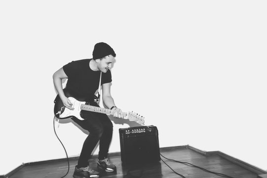 Awesome crazy fashion young musician rock guitar player jumps with passion in studio. Stylish rocky emotional man. Black and white toned.