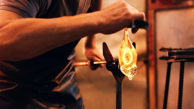 Glassblower reheating a piece of glass in furnace