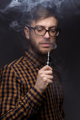 man with a beard wearing glasses on black background smoke Vape. large portrait of . electronic cigarette. E- for vaping. Popular devices  the year - modern device. Stop smoking,
