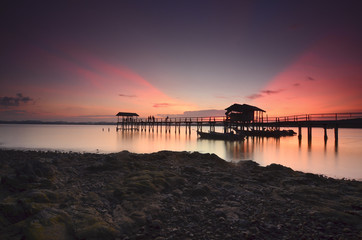 Beautiful sunset over wooden jetty with silhoutte of man fishing