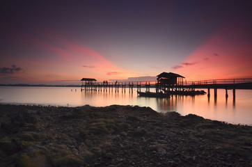 Fototapeta premium Beautiful sunset over wooden jetty with silhoutte of man fishing