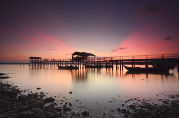 Fototapeta na wymiar Beautiful sunset over wooden jetty with silhoutte of man fishing