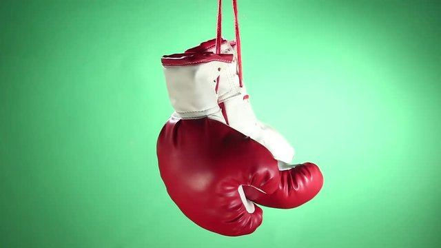 Boxing gloves hanging and rotating on green background.