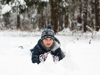 Fototapeta na wymiar Kid playing winter game. Boy lying on snow in the forest 