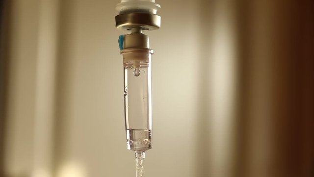 Slow motion focus on intravenous drip on defocused pale bright background, infusion dripping drops. Shallow depth of field isolated.