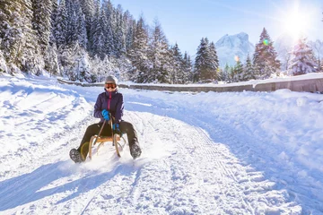 Fotobehang Cheerful girl riding a sled downhill, snow, sunny winter landscape © NicoElNino