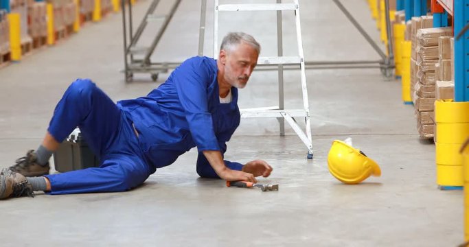 Male warehouse worker falling off ladder while working