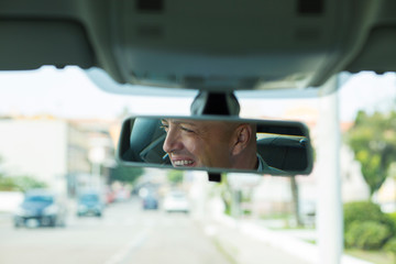 man driver looking at rear view mirror smiling,