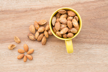 Almonds in yellow bowl on wooden background