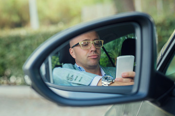 view side mirror reflection of man driver looking at phone, texting in car.