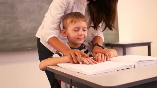 Teacher helping a blind schoolboy with his homework in classroom
