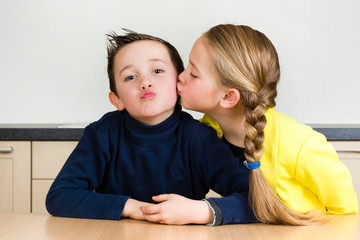 Pretty young girl gives little brother a kiss at home in the kitchen