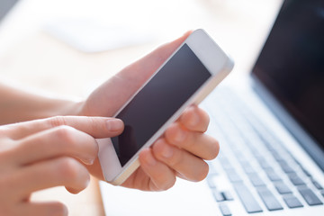 Hands using phone for searching, online shopping, business in front of laptop in simple interior