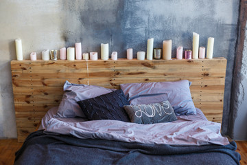 Stylish bedroom in loft style with grey colors and many candles. Bed with dark grey blanket