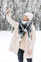 A young woman in a park full of snow, photographing her self by phone