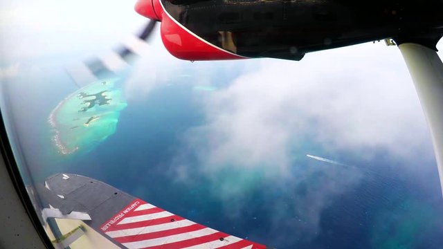 Engine of an otter twing water plane in action while flying above the maldives, showing amazing tiny colorful islands and unique turquoise color of the indian ocean. 