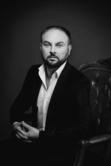 portrait of young man in black suit sitting on luxury chair on dark background