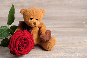 Obraz premium Valentine's day concept with Cute toy Bear with a red rose on wooden background. copy space