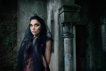 portrait of a girl in a pink dress and a black veil near the tomb in the cemetery