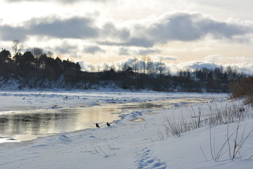 beautiful winter horizontal landscape: the river and the snow on a background of dark sky with clouds