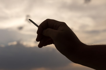 silhouette hand with a cigarette on a sunset background