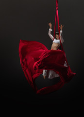 Pretty young gymnast on red aerial silks in studio