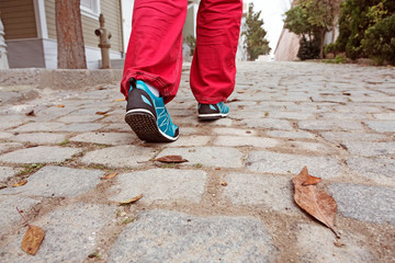Fototapeta na wymiar Human Feet walking on old paved Road with autumnal Leaves