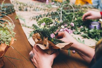 Woman's hands making flower composition at floristic workshop, DIY tools, branches. stems and twine...