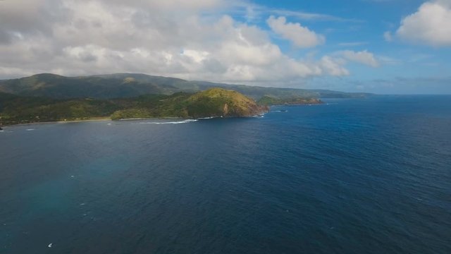 The coast of the tropical island with the mountains and the rainforest on a background of ocean with big waves.Aerial view: sea and the tropical island with rocks, beach and waves. Seascape: sky