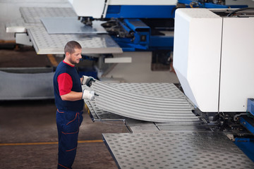 Inside a factory, industrial worker in action on metal press machine holding a piece of steel ready to be worked.