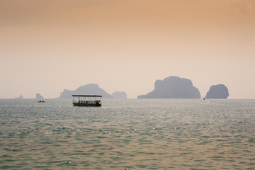 Naklejka na ściany i meble A boat and a kayak in the Andaman Sea near Ao Phra Nang Beach at dusk. In the background to the right Poda Island and to the left Chicken Island.