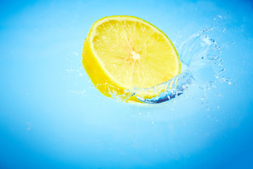 Fetta di limone cade nell'acqua con splash fondo blu