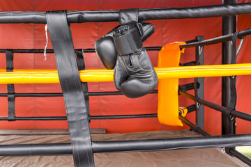 Black boxing gloves hang on hanging on ropes of ring.