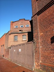Rostiges Stahltor einer ehemaligen Fabrik mit einer Fassade aus traditionellem braunem Backstein...