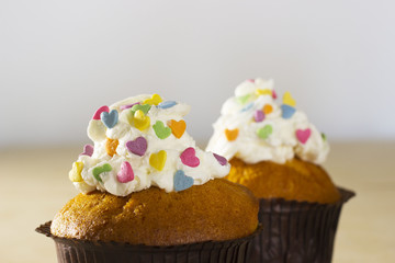 A two muffins with cream and decorative colored hearts on a light background